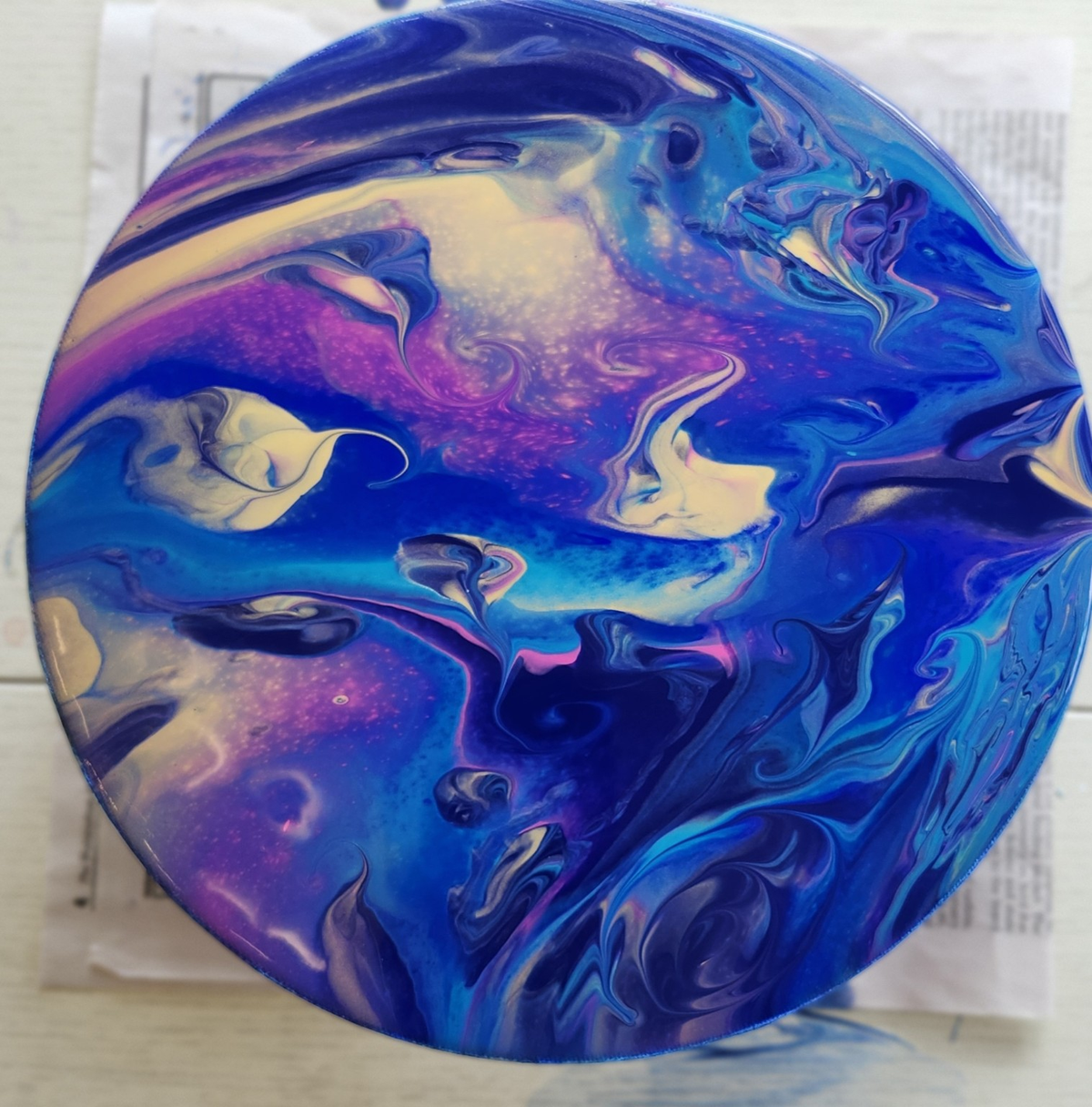Circular fluid art painting with swirling blue, purple, magenta, and cream tones